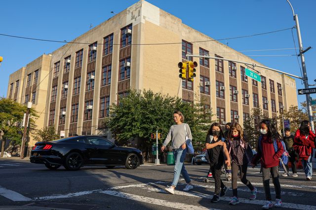 exterior of PS 166 in Queens,  seeing the building from across the street with children crossing the street in the foreground